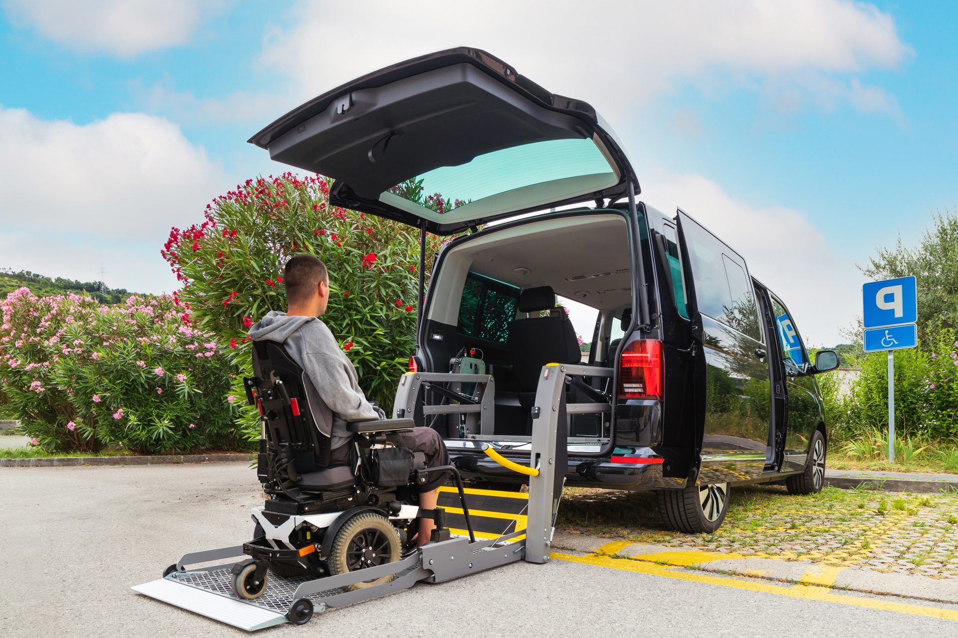 Photo d'une personne en fauteuil motorisé utilisant un ascenseur derrière un véhicule adapté